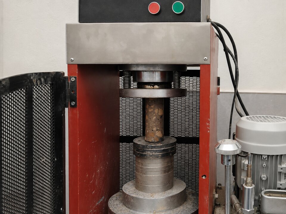 Equipo de laboratorio aplicando compresión a una probeta cilíndrica.